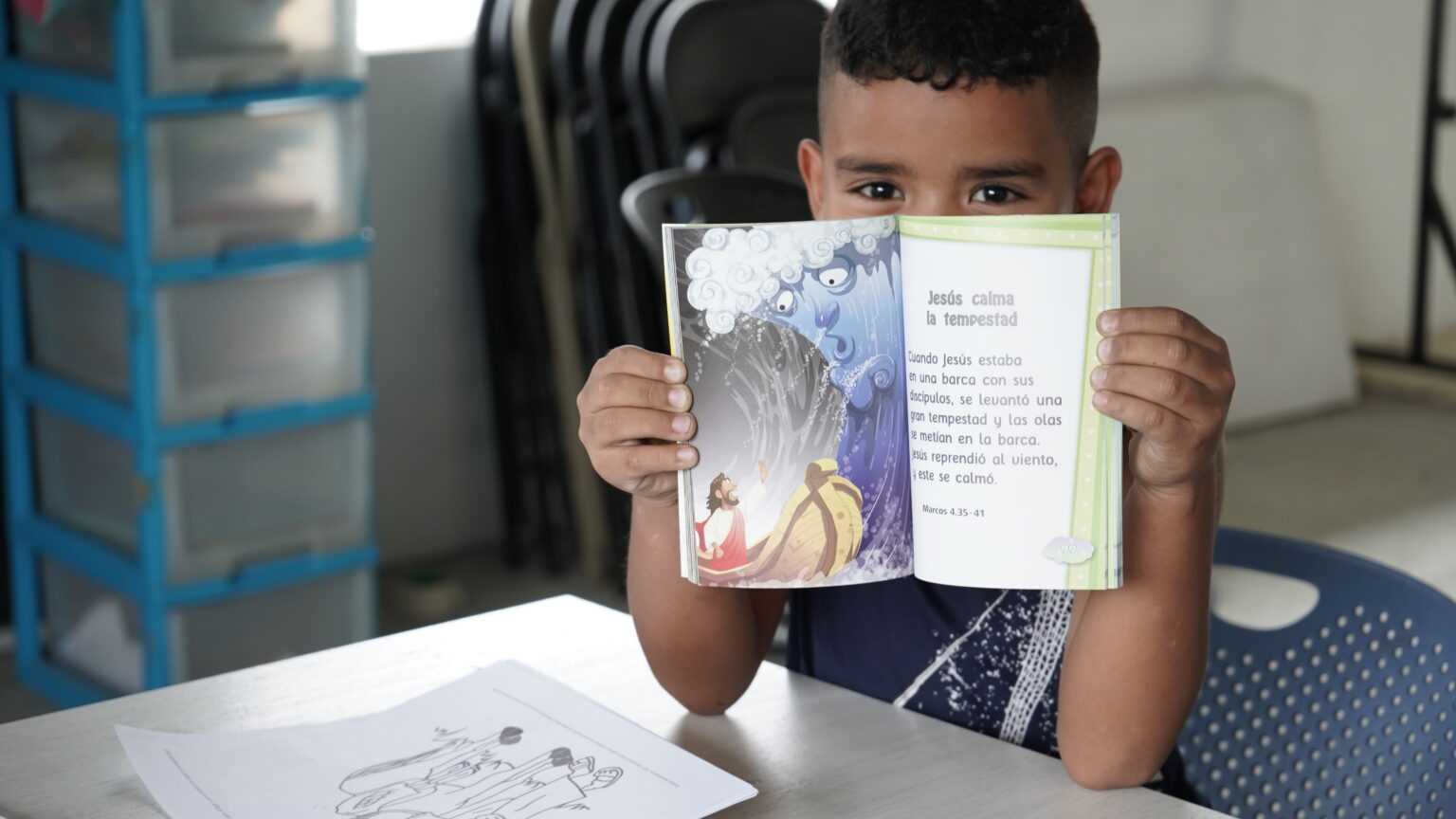 Niño lee una Biblia infantil ilustrada abierta en «Jesús calma la tempestad»